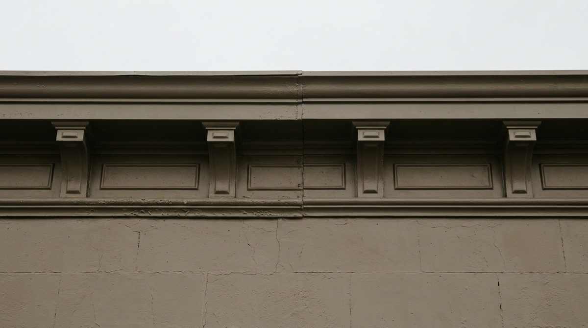 A pressed sheet metal cornice with repeating brackets under a plain roofline, painted, in flat daylight